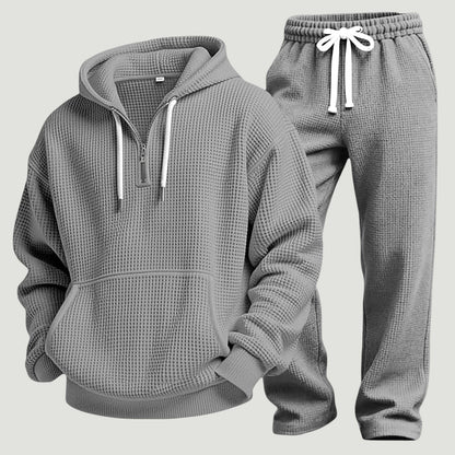 Grått set av våffelstickad huvtröja med halv dragkedja och joggingbyxor med vitt dragsnöre, fristående produktbild. 10