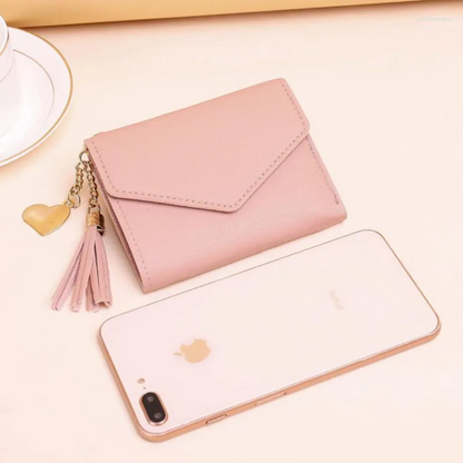 Rosa Mini-Geldbörse mit Quastenanhänger aus Leder neben Smartphone auf Tisch.