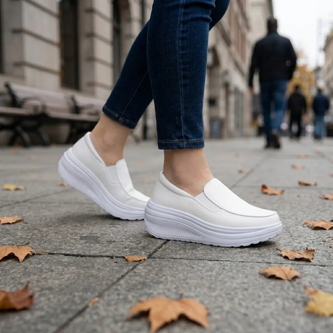 Vita instegsskor på en modell i jeans som går på stenlagd gata med höstlöv 11