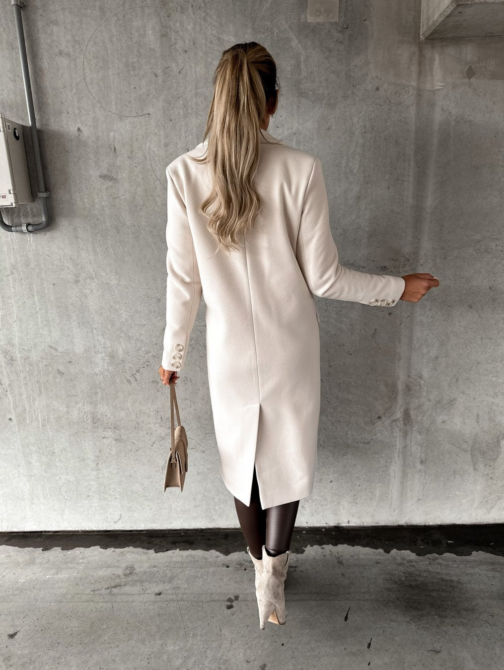 Frau in weißem Wollmantel mit langen Ärmeln, hält beige Handtasche, Herbstmode 2022.