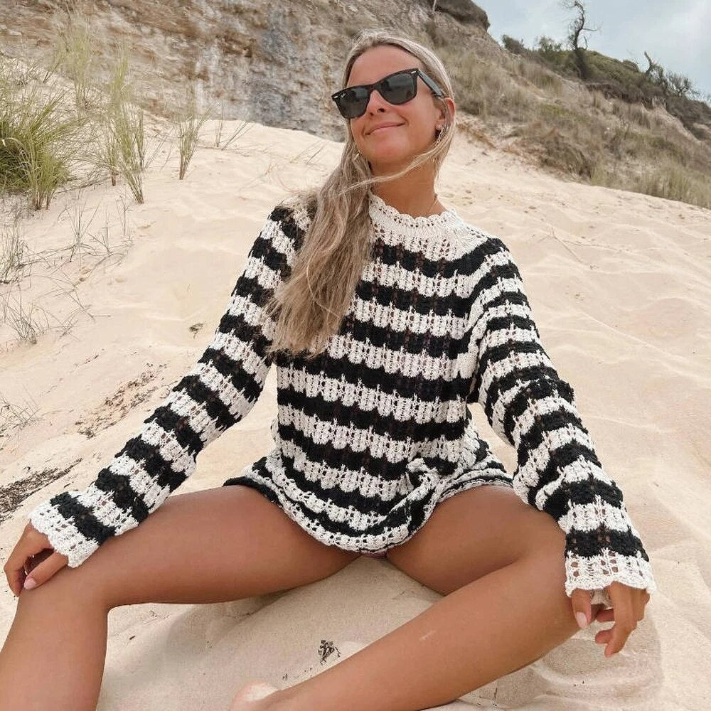 Frau in gestreiftem Strickpulloverkleid am Strand, schwarz-weiß, lässig, modisch.