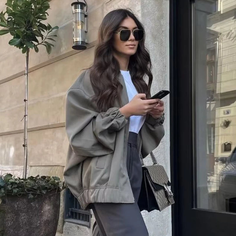 Frau in übergroßer, grauer Herbstjacke mit Smartphone und Sonnenbrille auf der Straße.
