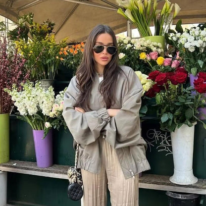 Frau in übergroßer grauer Jacke vor Blumenstand, Herbstmode, lässiger Stil.