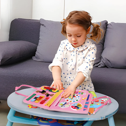 Liten flicka i klänning trycker på klockan och vridskivorna i den rosa boken vid ett bord 5