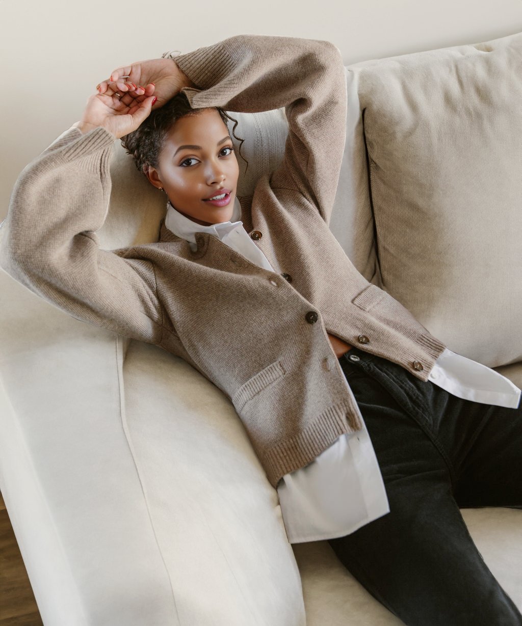Frau in beigem Button-Up-Cardigan auf Sofa, lässige Mode, gemütlicher Look.