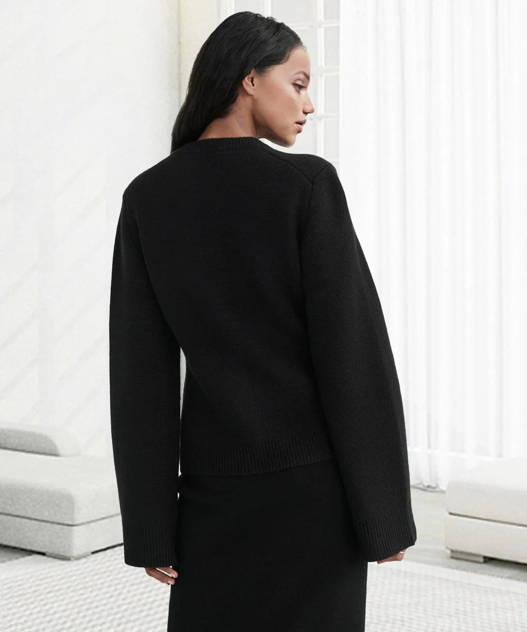 Frau in schwarzem Strickpullover, langärmelig, elegantes Design, vor weißem Hintergrund.