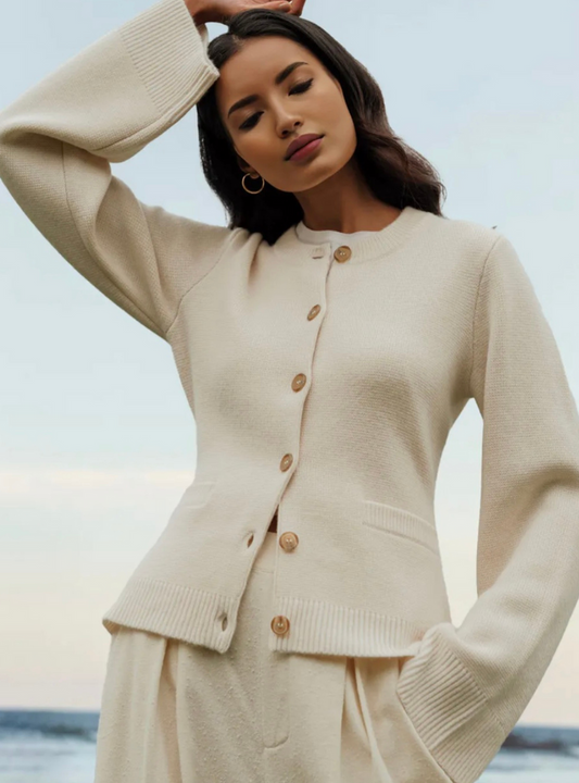 Frau in cremefarbenem Button-Up-Strickpullover am Strand, weiches Material, modisch, elegant.