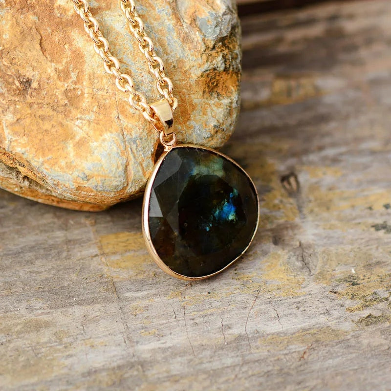 Labradorit Tropfenanhänger, goldene Kette, natürlicher Edelstein, Schmuck, rustikaler Hintergrund.