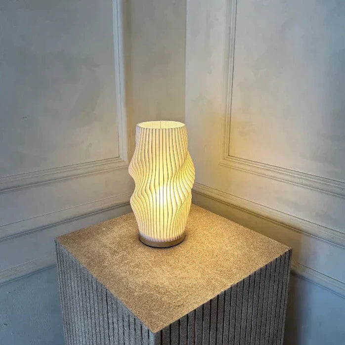 Moderne Tischlampe mit weißem, wellenförmigem Lampenschirm auf rechteckigem Sockel, minimalistisch.