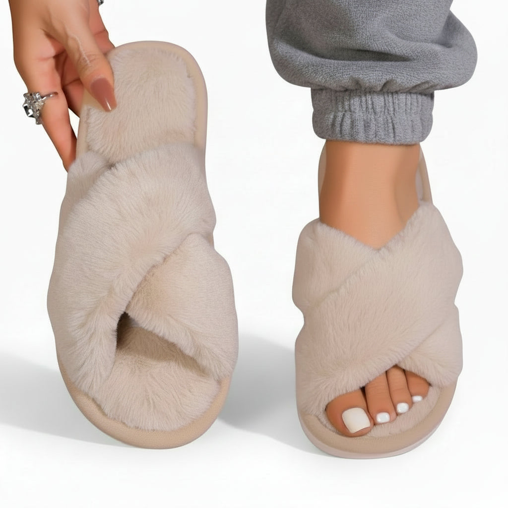Ljusbeige fluffiga innesandaler, den ena hållen i handen med synlig vadderad innersula, den andra buren med grå mjukisbyxor. 7