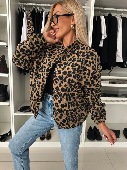 Modell i leopardmönstrad bomberjacka med stor krage och knappar, vinklad framifrån med handen mot ansiktet, ihop med jeans och svart linne. 1
