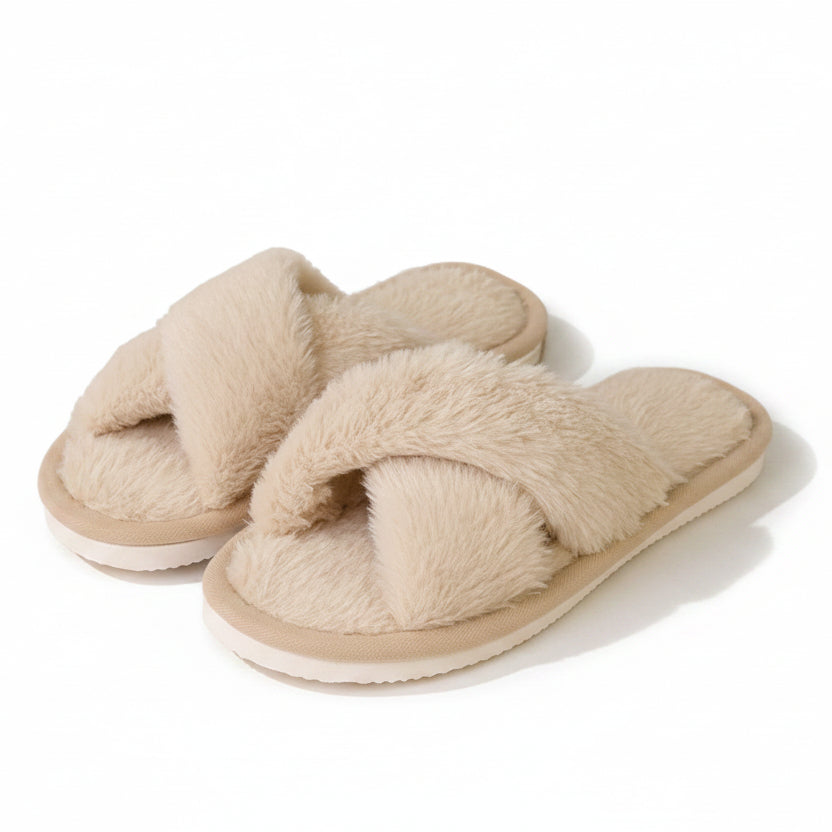 Ett par beige innesandaler i lurvigt, mjukt material med korsade remmar, fotograferade snett framifrån mot vit bakgrund. 1