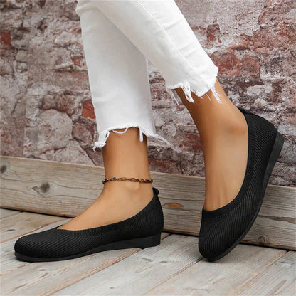Schwarze Damen-Ballerinas aus Mesh, flach, bequem, modisch, vor Backsteinwand.