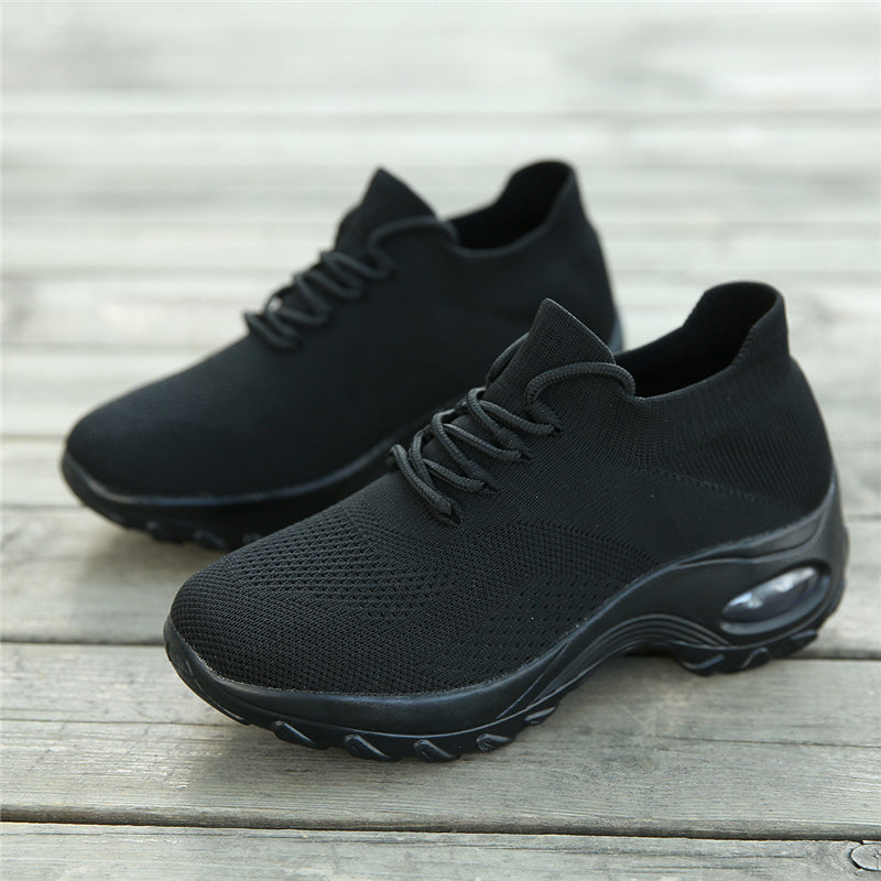 Schwarze Sportschuhe mit atmungsaktivem Mesh-Obermaterial auf Holzboden.