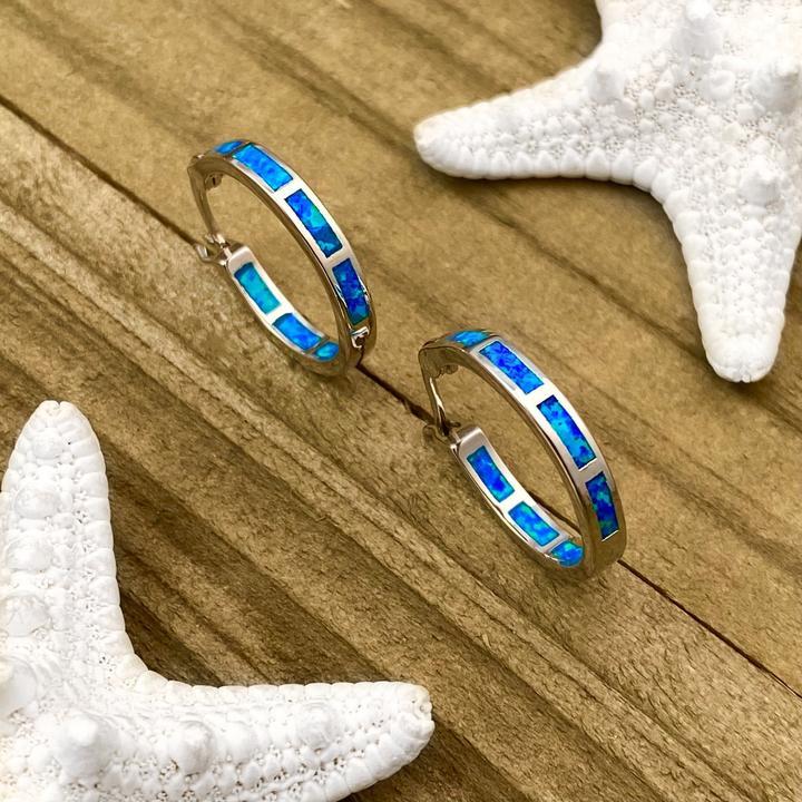 Opal-Ohrringe mit blauem Schimmer auf Holzuntergrund, dekoriert mit weißen Seesternen.