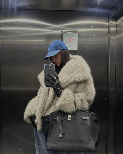 Frau im Aufzug mit Pelzmantel, blauer Kappe, schwarzer Lederhandtasche, Smartphone in der Hand.