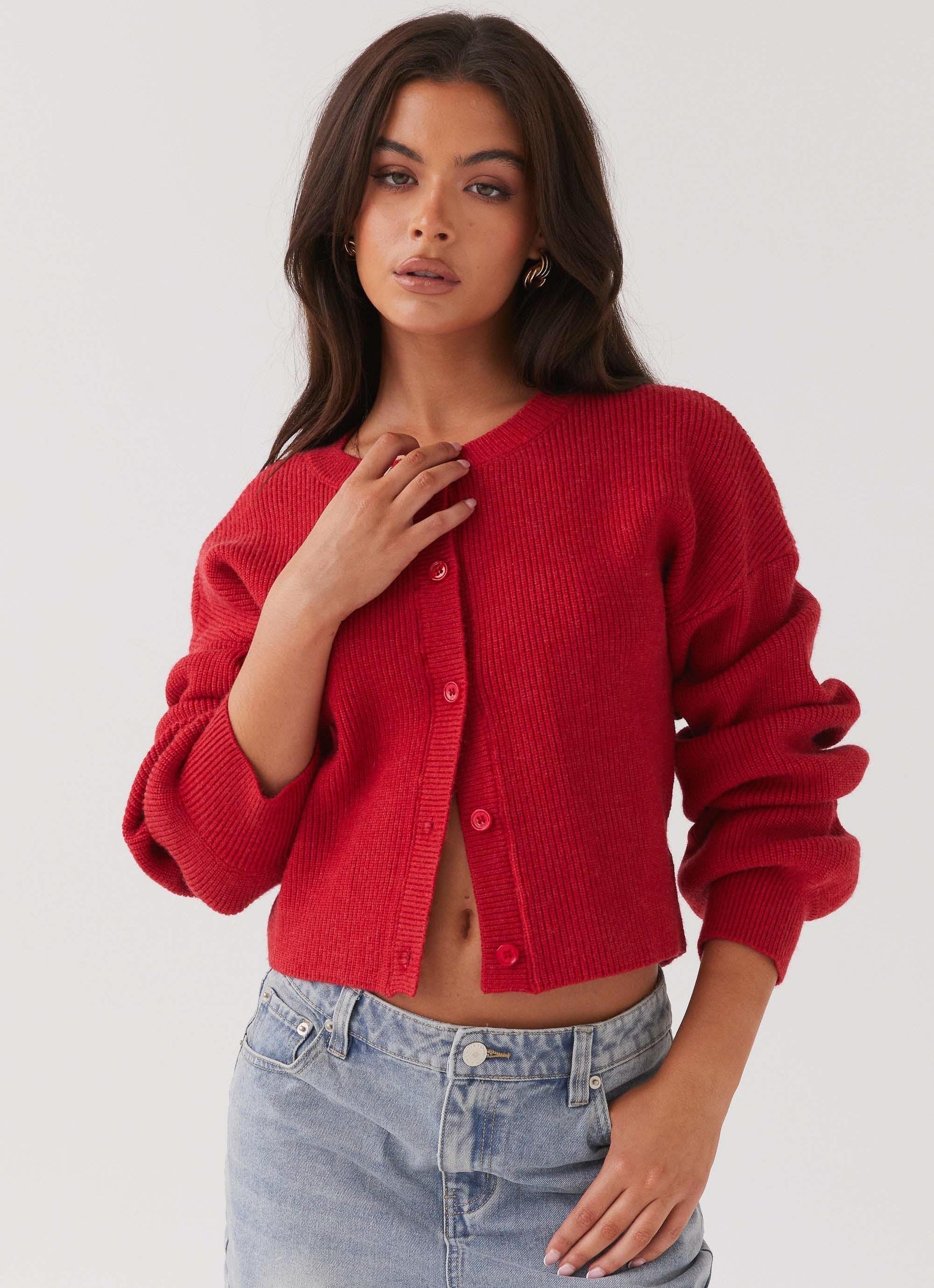 Frau trägt roten Strickcardigan, lange Ärmel, Knopfleiste, kombiniert mit blauer Jeans.