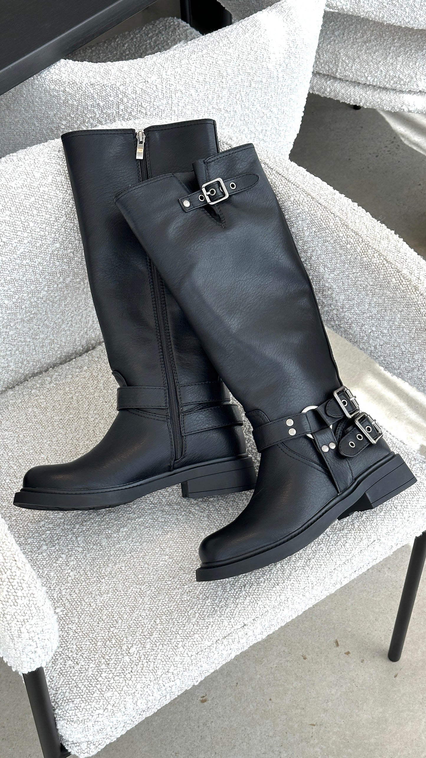 Schwarze Lederstiefel mit Schnallen auf einem weißen Sessel, modisch und elegant.