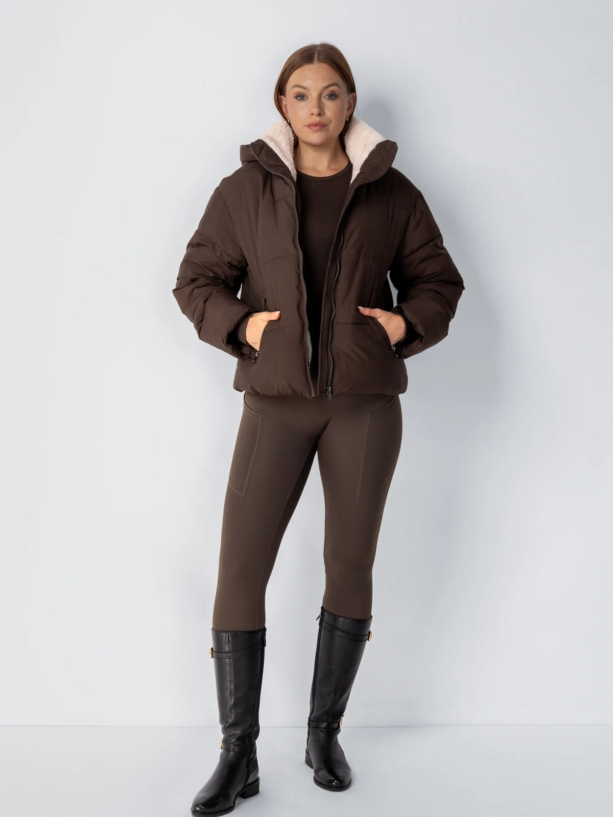 Helbild av modell i mörkbrun jacka med teddyfoder, brun outfit och svarta höga stövlar 15