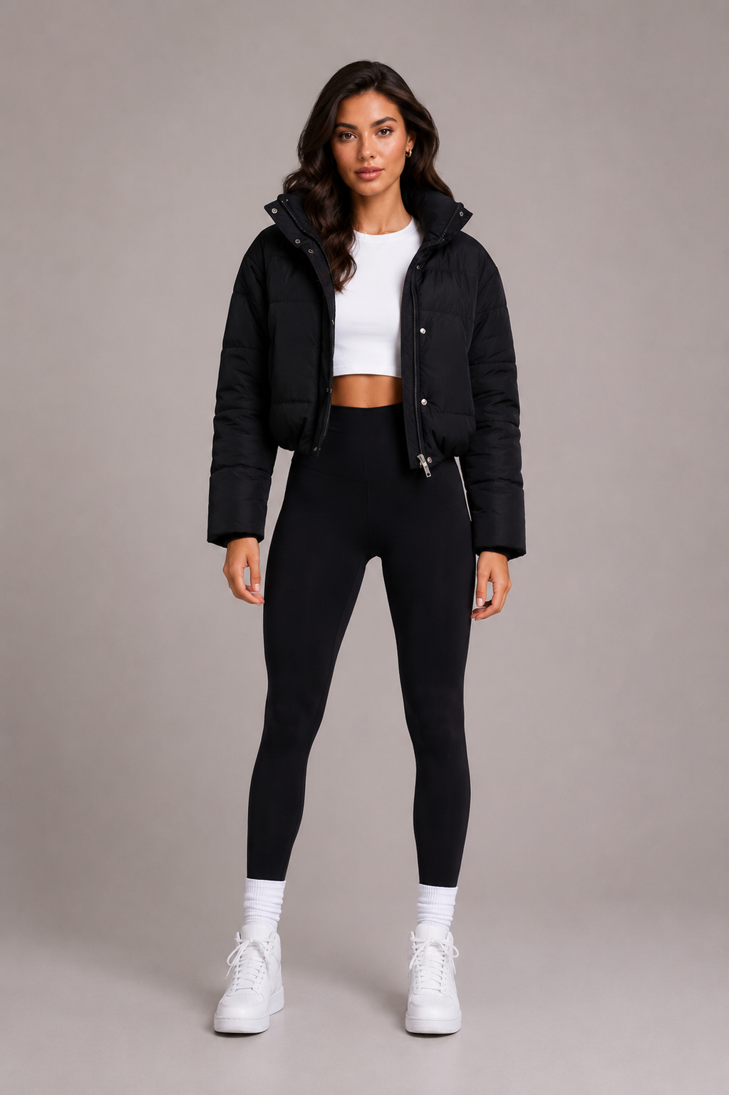 Modell i helfigur framifrån bär den svarta korta puffjackan med stående krage, vitt linne, svarta leggings och vita sneakers. 2