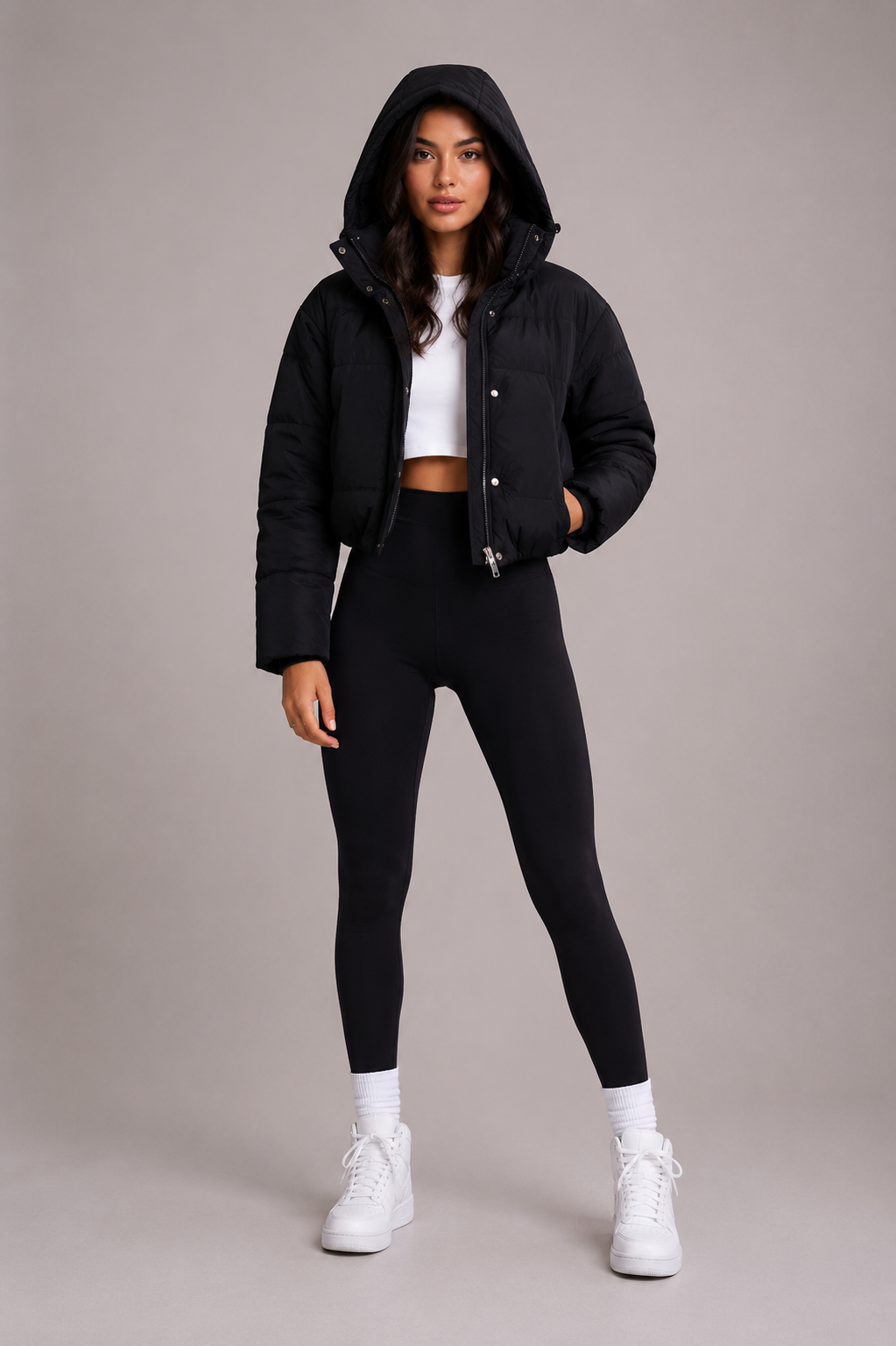 Modell i helfigur med huvan uppdragen över huvudet och ena handen i fickan, klädd i svarta leggings och vita sneakers. 3