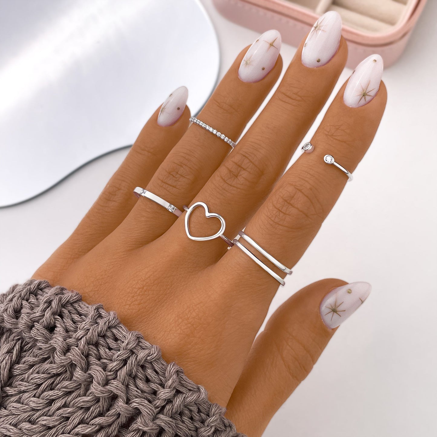 Damenhand mit silbernen Ringen, Herzdesign, Strickpullover, Nageldesign mit Sternen.