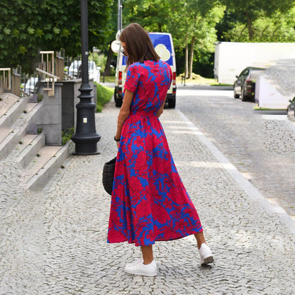 Frau im rot-blauen Blumenkleid auf Kopfsteinpflasterstraße, Sommermode, Freizeitkleidung.