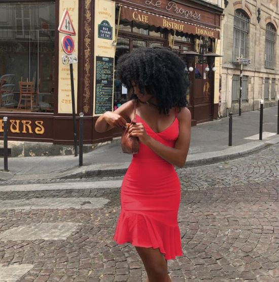 Frau in rotem Kleid auf Kopfsteinpflasterstraße vor Café in Paris.