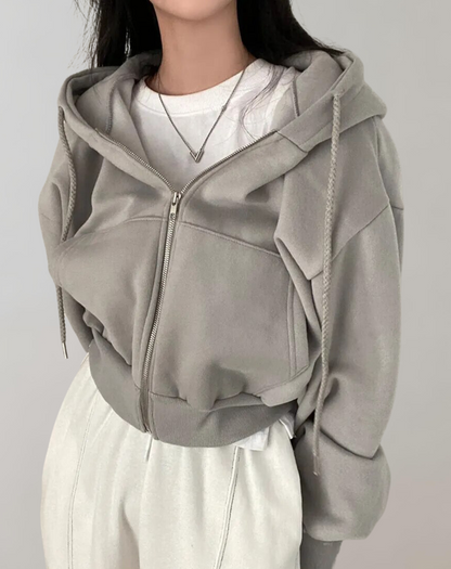 Modell i grå kort hoodie med dragkedja och flätade dragsnören, ribbad nederkant, över vit tröja och vita byxor. 4