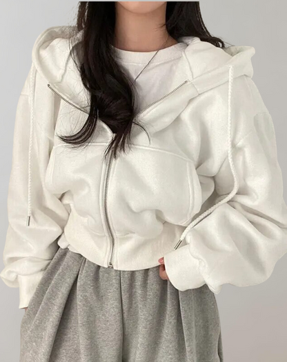 Modell i vit hoodie med öppen dragkedja och dragsnören, bärd över vit tröja och grå mjukisbyxor, sedd framifrån och nära. 1