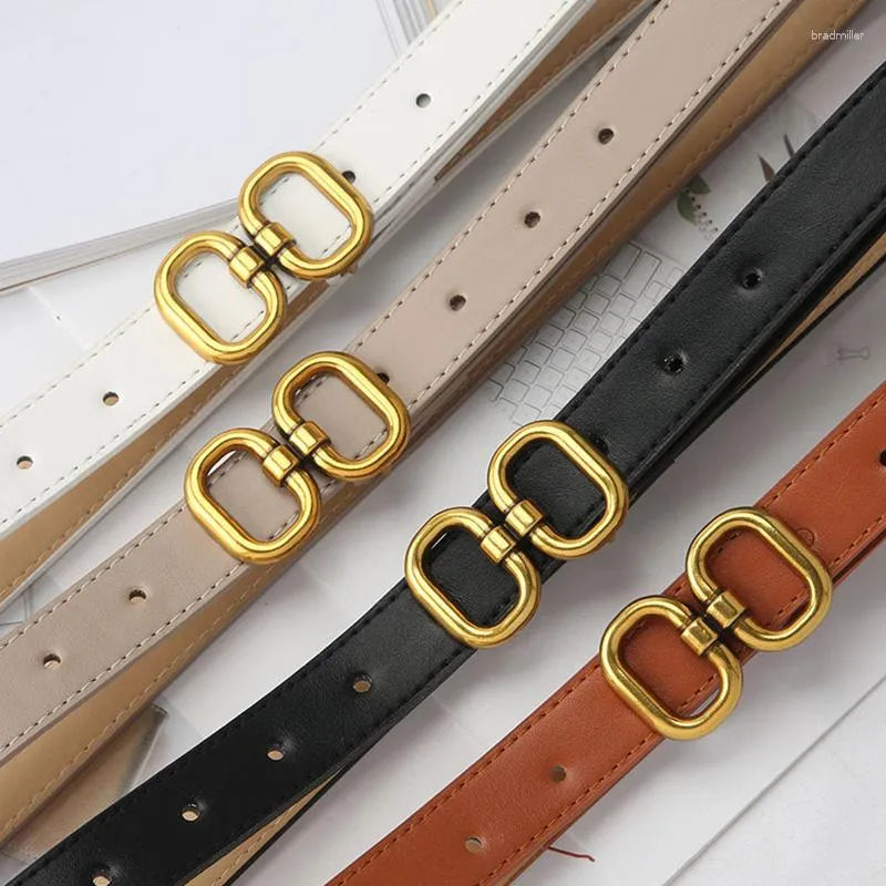 Vier Retro-Gürtel mit goldener Schnalle in Weiß, Beige, Schwarz und Braun auf einem Tisch.