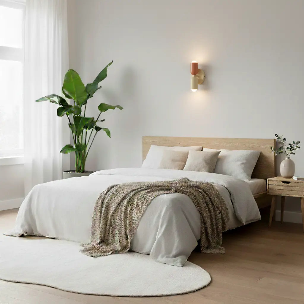 Lampa i korall och guld tänd ovanför en bäddad säng med vita sängkläder, stor krukväxt och rund matta. 8