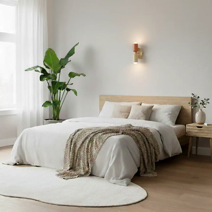 Lampa i korall och guld tänd ovanför en bäddad säng med vita sängkläder, stor krukväxt och rund matta. 8