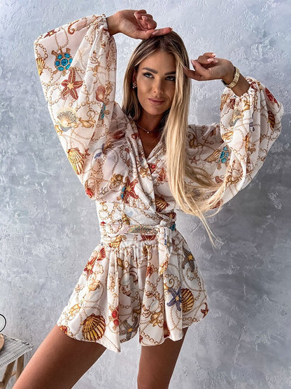 Frau in weißem, gemustertem Sommerkleid mit langen Ärmeln vor grauer Wand.