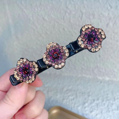 Närbild på en hårklämma med tre blommor i strass i lila, rosa och guldbeige nyanser, hållen i handen. 2