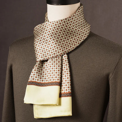 Beige halsduk med små orangebruna cirkelmotiv, mönstrad bård och ljusgul slät kant, draperad på skyltdocka med olivgrön tröja. 9