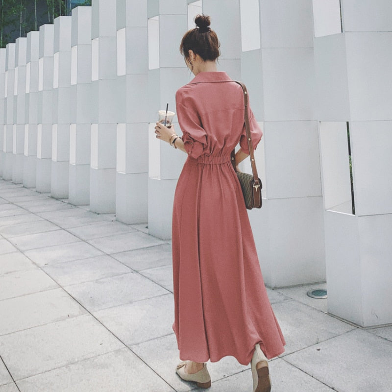 Frau in rosa Maxikleid mit Kaffeebecher, moderne Architektur, lässiger Stadtstil