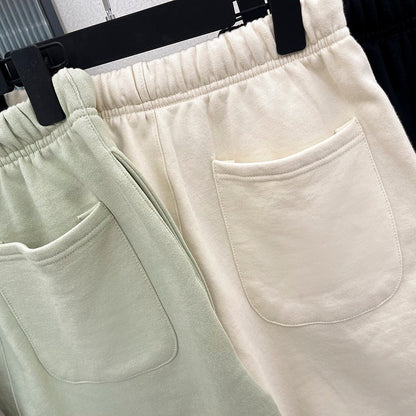 Zwei Jogginghosen aus Baumwolle, eine in Mintgrün, eine in Cremeweiß, mit Taschen, auf Kleiderbügel.
