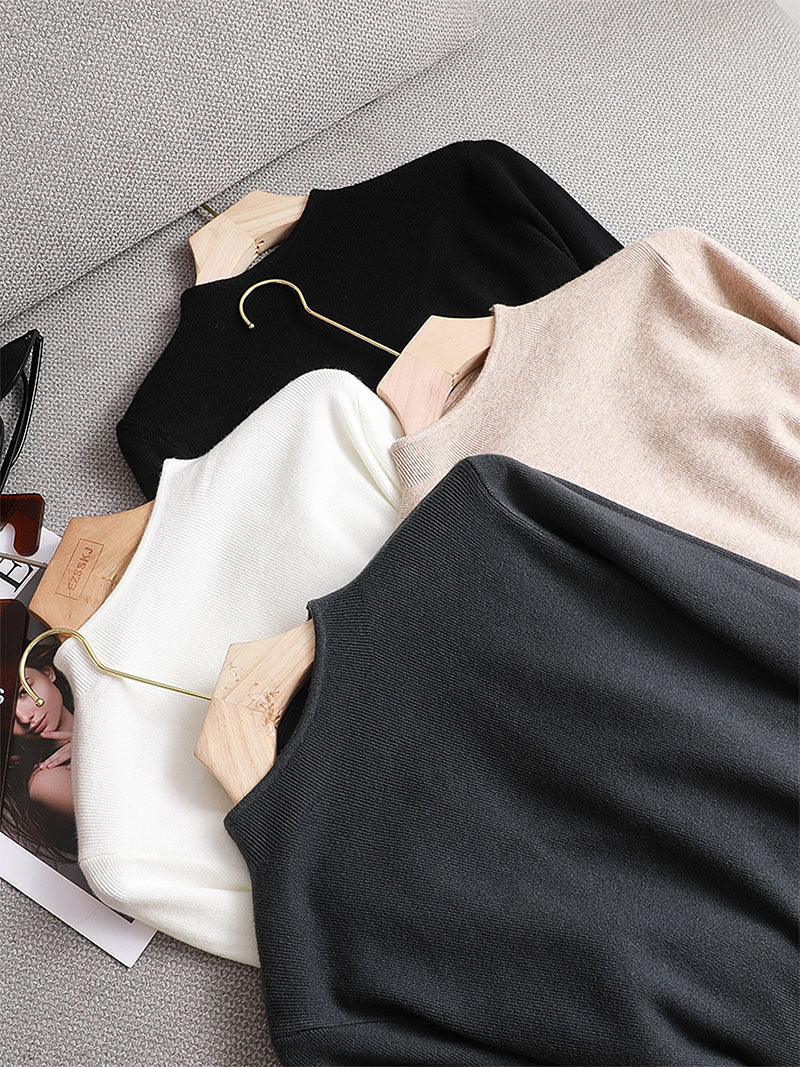 Vier Pullover in Schwarz, Weiß, Beige und Grau auf einem Sofa, aus Baumwolle, modisch, elegant.