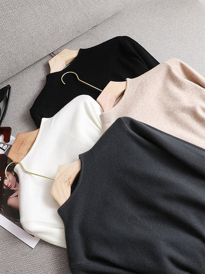 Vier Pullover in Schwarz, Weiß, Beige und Grau auf einem Sofa, aus Baumwolle, modisch, elegant.