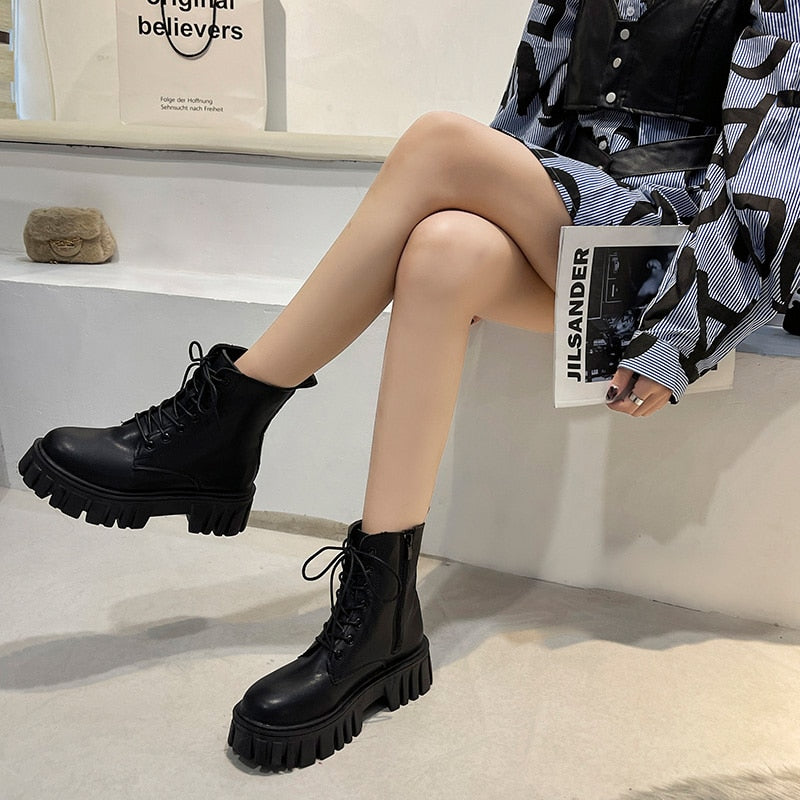 Frau trägt schwarze Lederstiefel mit dicker Sohle, modisches Outfit, sitzt auf Bank.