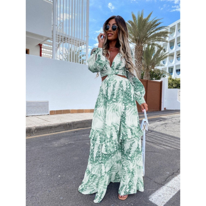 Frau in langem, grün-weißem Sommerkleid mit Blattmuster, Sonnenbrille, draußen, Palmen im Hintergrund.