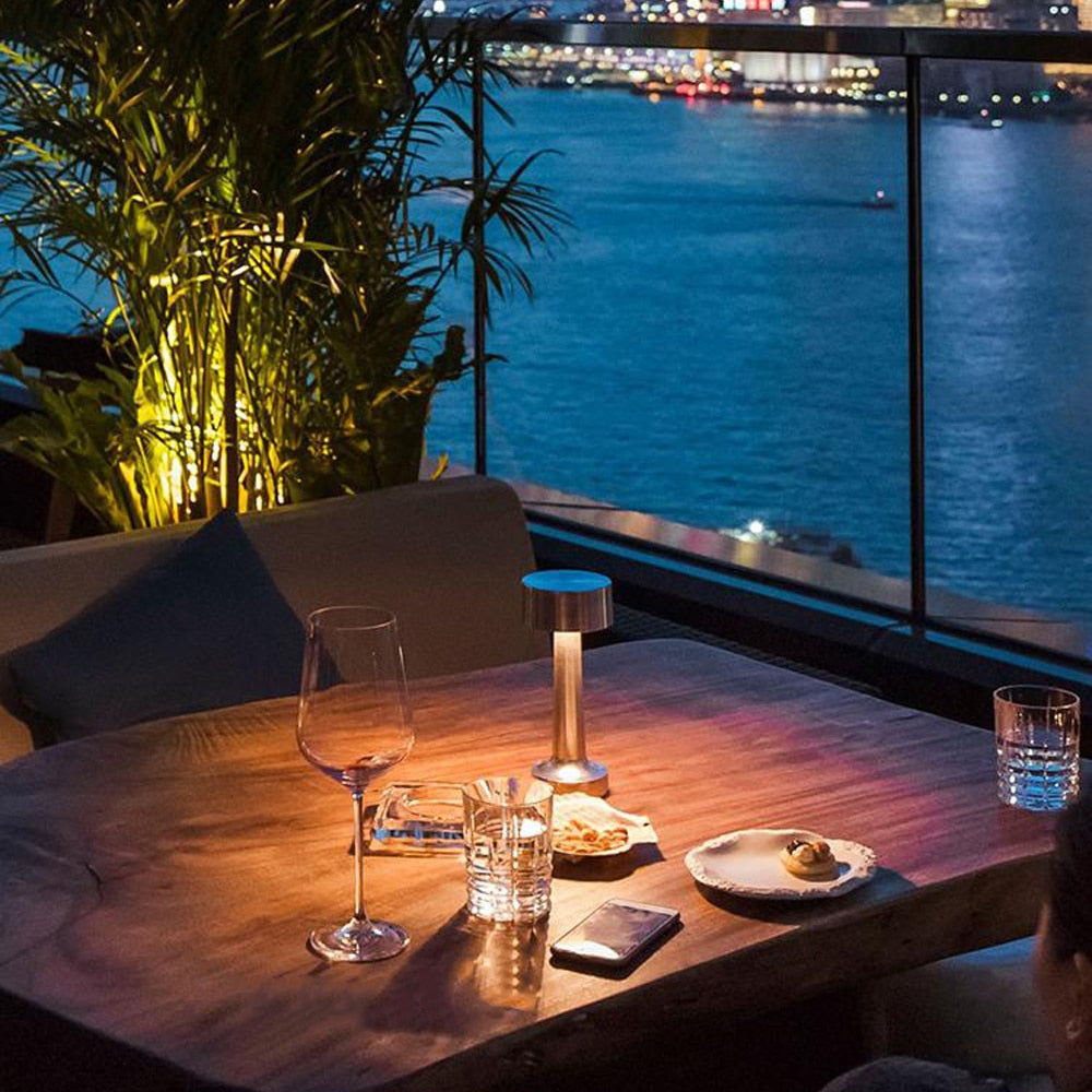 Gemütlicher Abend auf Terrasse mit Holztisch, Weinglas, LED-Lampe, Blick auf beleuchtete Stadt.