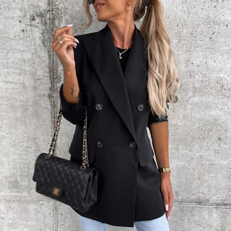 Frau in schwarzem Blazer mit gesteppter Handtasche, blonde Haare, lässiger Stil.