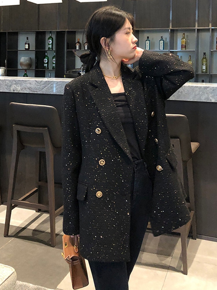 Frau in schwarzem Blazer mit goldenen Knöpfen in moderner Barumgebung.