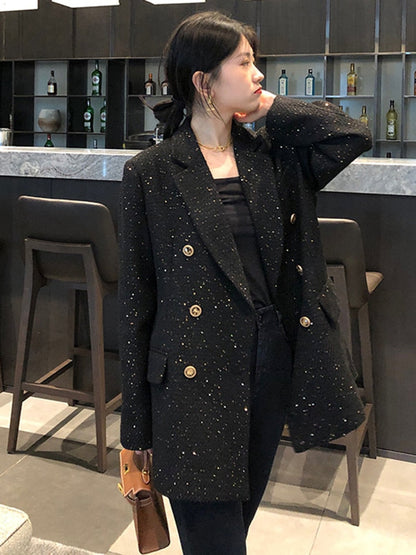 Frau in schwarzem Blazer mit goldenen Knöpfen in moderner Barumgebung.