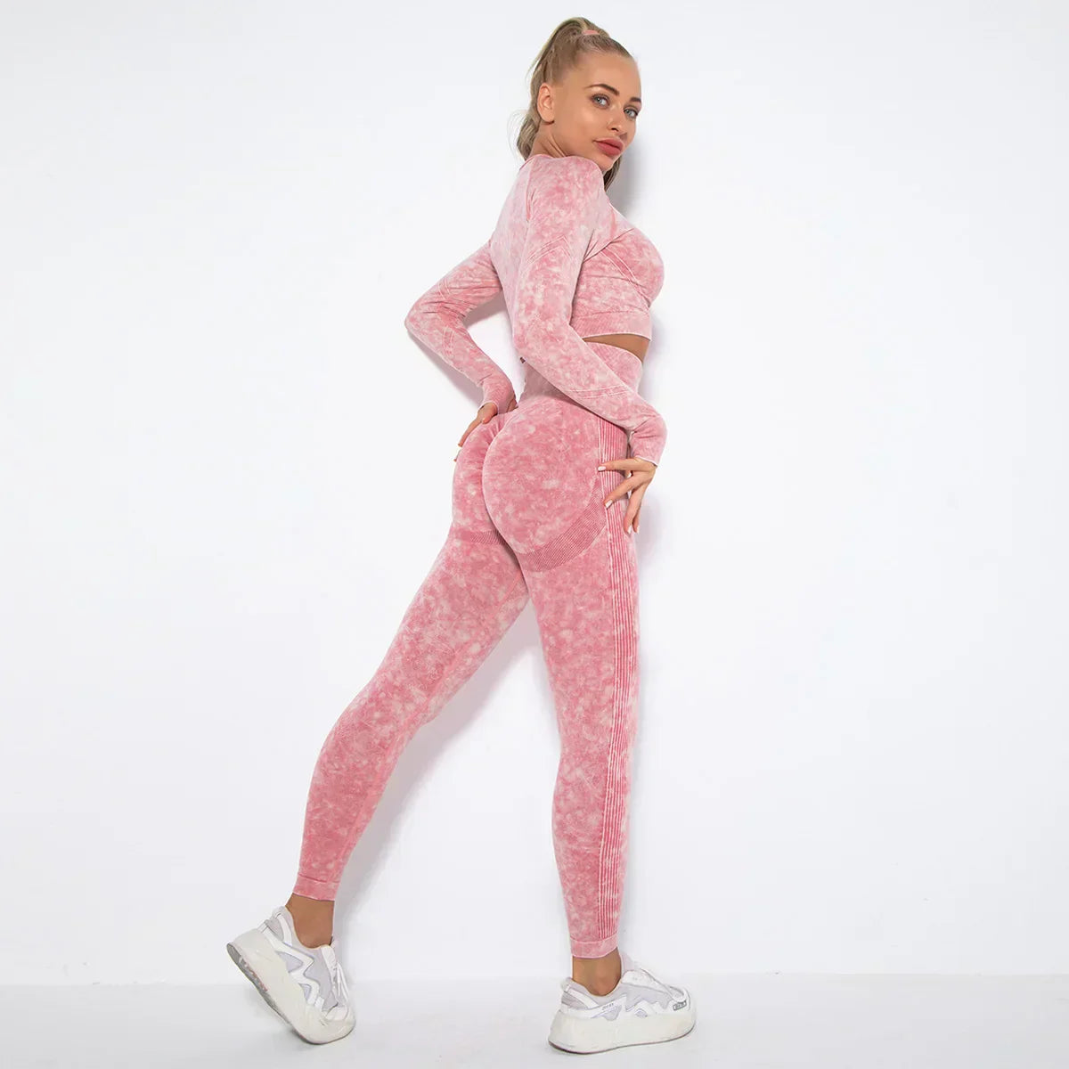 Frau in rosa nahtlosem Sport-Set, langärmeliges Oberteil, Leggings, weiße Sneaker, Fitnessmode.