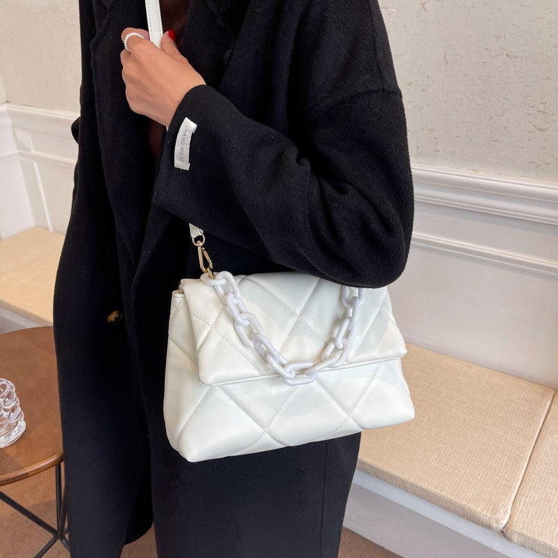 Weiße gesteppte Handtasche mit Kettengurt, getragen von Person in schwarzem Mantel.