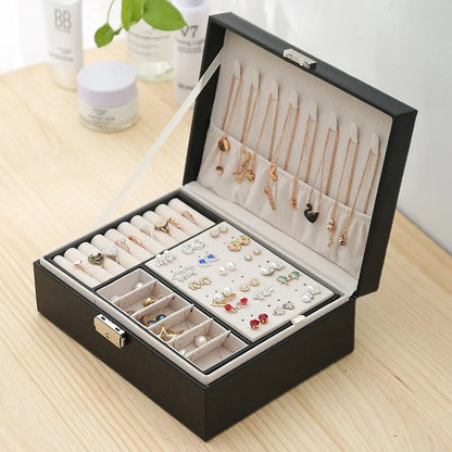 Schwarze Schmuckbox mit Fächern für Ohrringe, Ringe und Ketten auf Holztisch.