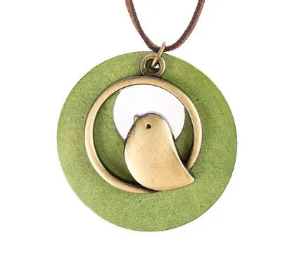 Runder Anhänger mit Vogelmotiv, bronzefarben, auf grünem Hintergrund, an braunem Lederband.